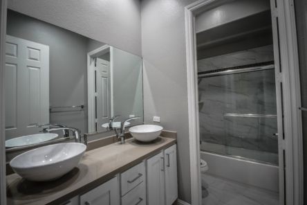 Contemporary guest bathroom renovation in Tujunga with double vessel sinks, custom cabinetry, and marble-look shower surround