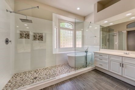Modern bathroom renovation with glass-enclosed shower, elegant subway tile, and freestanding tub positioned beneath bright window